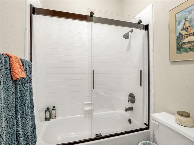 bathroom with a textured wall, toilet, and bath / shower combo with glass door