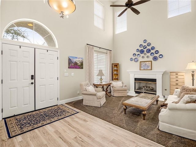 foyer entrance featuring baseboards, a glass covered fireplace, a towering ceiling, ceiling fan, and wood finished floors