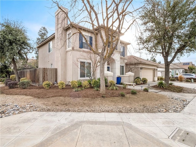 view of front of house with concrete driveway, a chimney, an attached garage, fence, and stucco siding