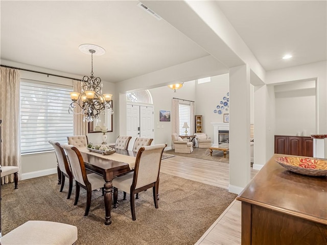 dining room with a chandelier, light wood-style flooring, visible vents, baseboards, and a glass covered fireplace