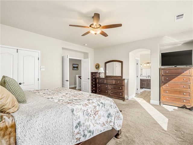 bedroom featuring arched walkways, visible vents, a ceiling fan, light carpet, and connected bathroom