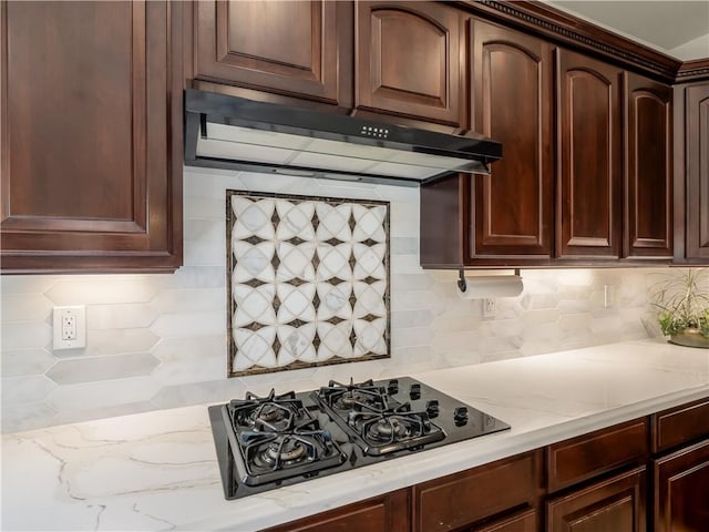 kitchen with black gas cooktop, light stone counters, backsplash, and under cabinet range hood