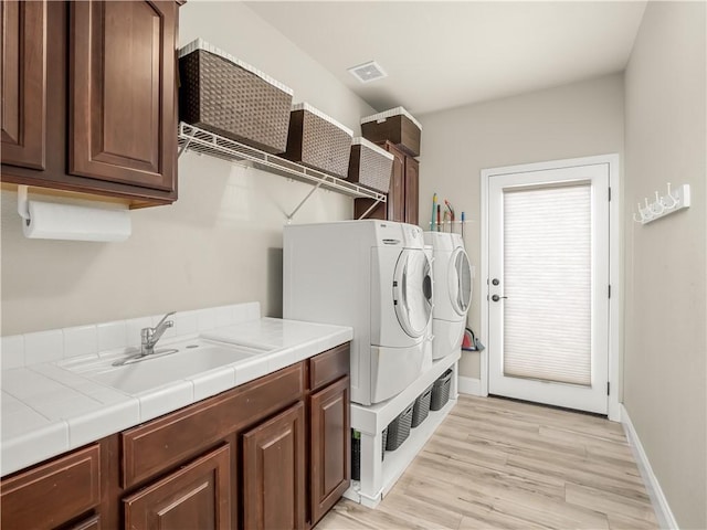 washroom featuring light wood-style flooring, a sink, visible vents, independent washer and dryer, and cabinet space