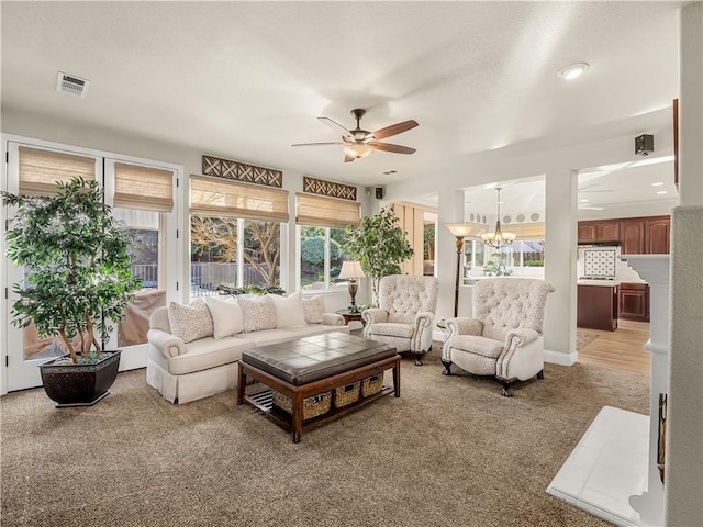 living room featuring ceiling fan with notable chandelier, visible vents, and light colored carpet