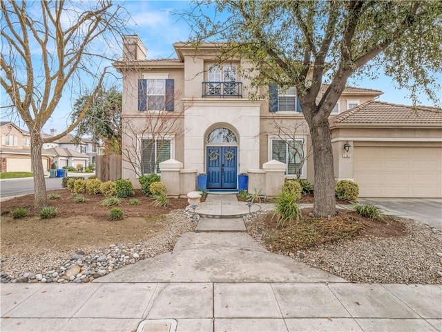 view of front of house with a balcony, driveway, french doors, stucco siding, and a chimney