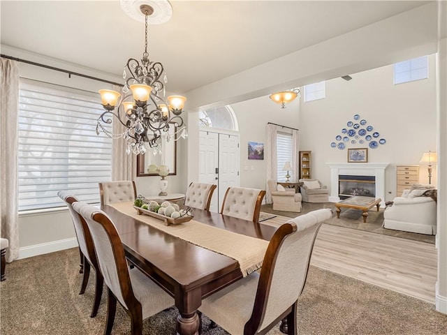 carpeted dining space featuring a chandelier, a wealth of natural light, a glass covered fireplace, and baseboards