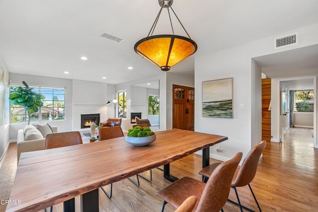 dining room with light wood-type flooring, a brick fireplace, and visible vents