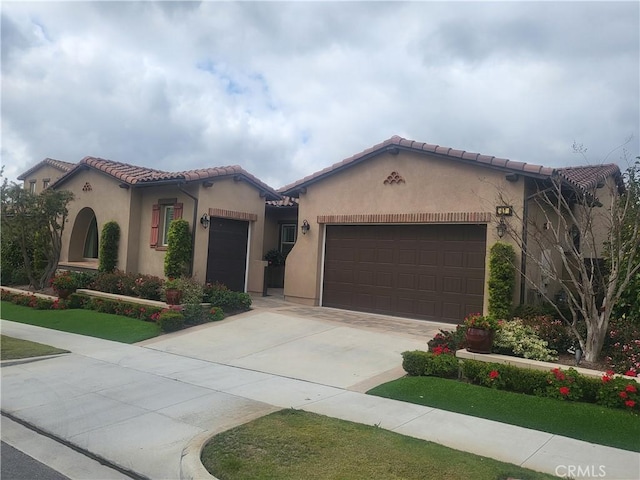 mediterranean / spanish home featuring a garage, concrete driveway, a tiled roof, and stucco siding