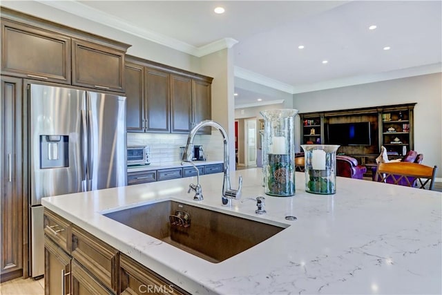 kitchen with light stone countertops, stainless steel fridge with ice dispenser, ornamental molding, decorative backsplash, and a sink