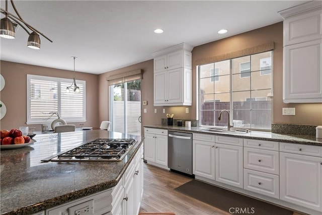 kitchen featuring stainless steel appliances, a sink, white cabinetry, light wood-type flooring, and pendant lighting