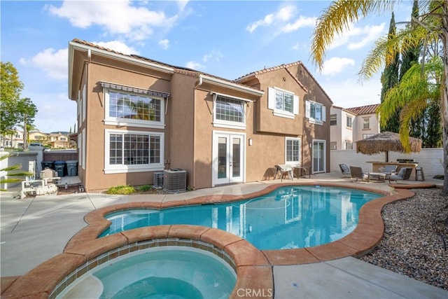 rear view of property featuring an outdoor pool, an in ground hot tub, french doors, a patio area, and stucco siding