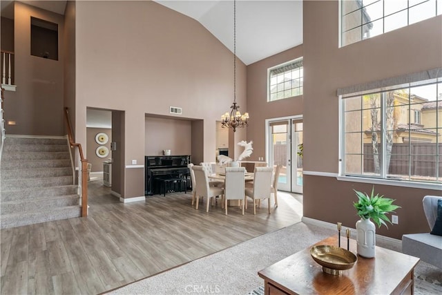 living room with a chandelier, light wood-style flooring, visible vents, baseboards, and stairway