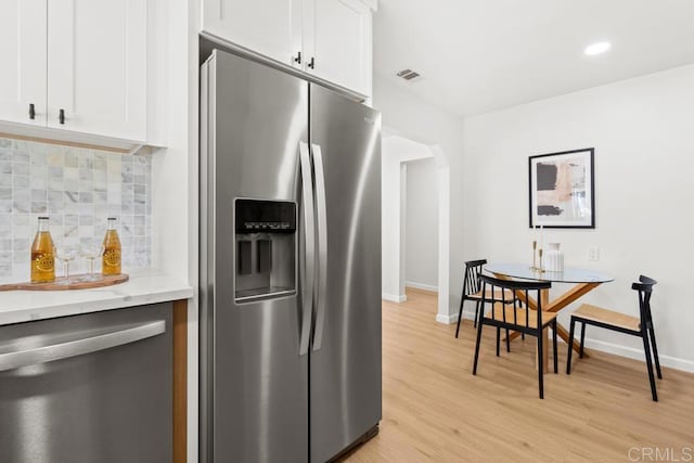 kitchen with white cabinets, light wood-style flooring, light stone countertops, stainless steel appliances, and backsplash