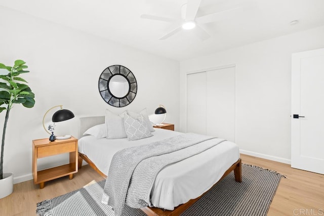 bedroom featuring ceiling fan, a closet, light wood-style flooring, and baseboards