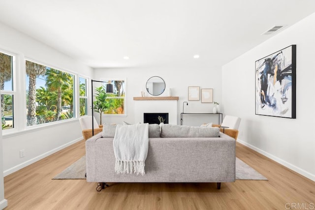 living room with visible vents, a fireplace, light wood-style flooring, and baseboards