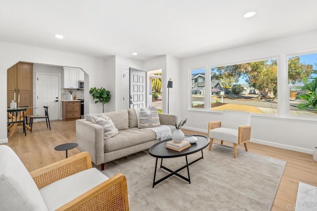 living room with baseboards, recessed lighting, arched walkways, and light wood-style floors