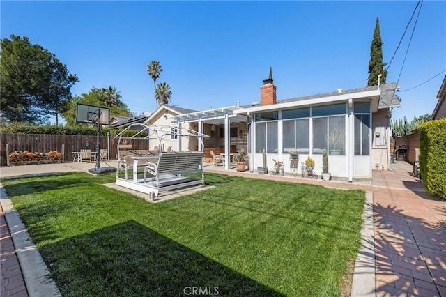 back of house featuring a yard, a chimney, a sunroom, a patio area, and a fenced backyard