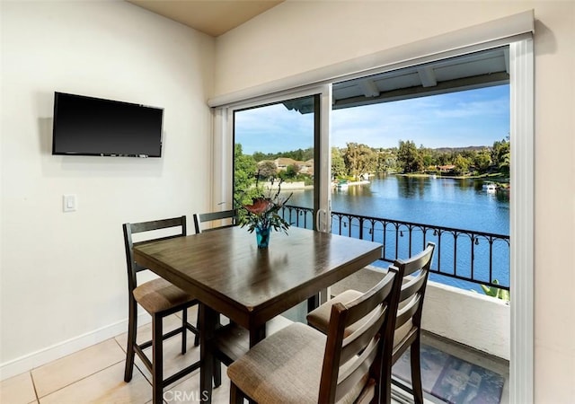 dining space featuring light tile patterned floors, a water view, and baseboards