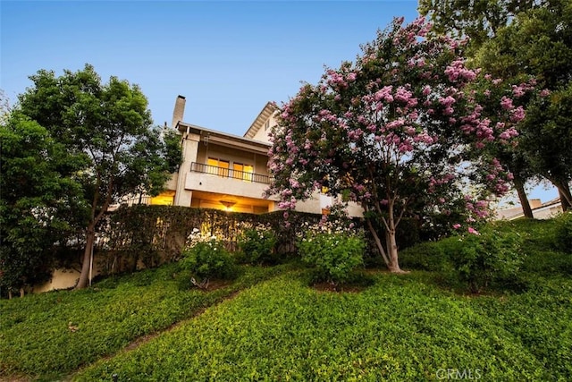 exterior space featuring a lawn, a chimney, and a balcony