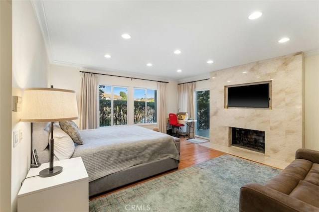 bedroom featuring wood finished floors, access to outside, crown molding, a fireplace, and recessed lighting