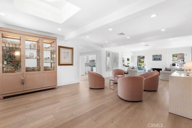 living area featuring light wood finished floors, a warm lit fireplace, a skylight, beamed ceiling, and recessed lighting