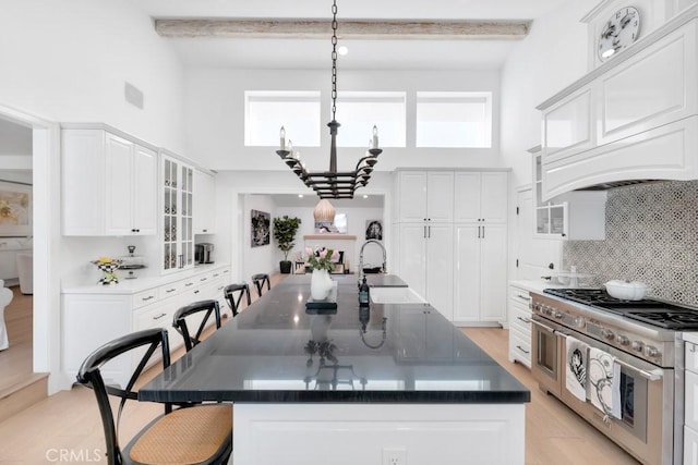 kitchen featuring range with two ovens, a breakfast bar, white cabinets, decorative backsplash, and beamed ceiling