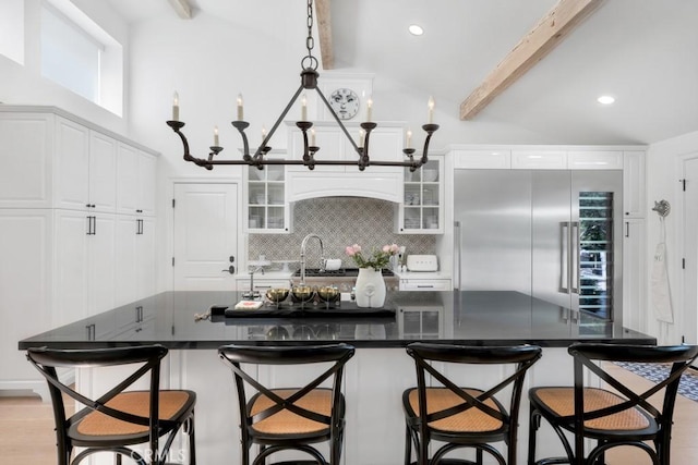 kitchen featuring dark countertops, white cabinets, beamed ceiling, and backsplash