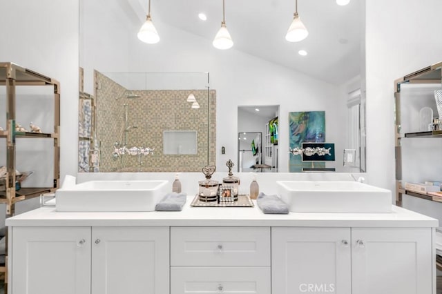 ensuite bathroom with lofted ceiling, tiled shower, a sink, and double vanity