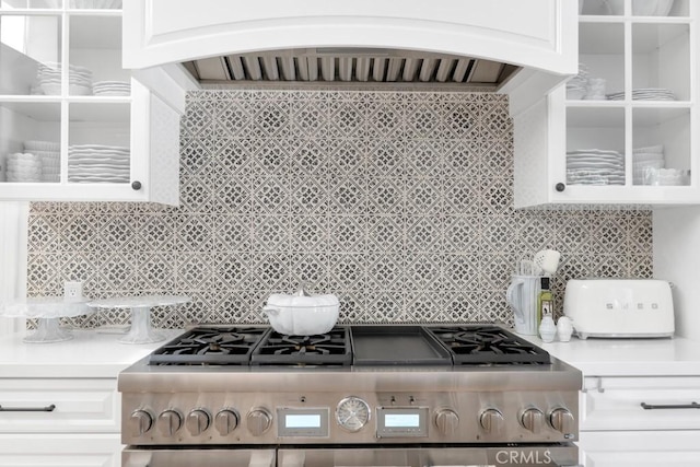 kitchen with stainless steel range, white cabinets, custom range hood, glass insert cabinets, and backsplash