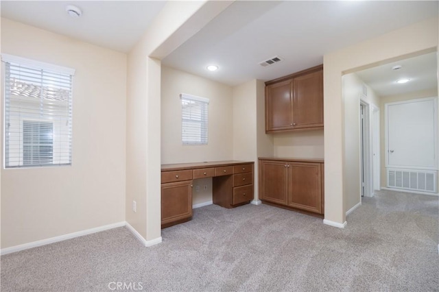 unfurnished office featuring light carpet, built in study area, visible vents, and baseboards