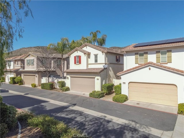 view of front of property featuring a garage, a tile roof, a residential view, roof mounted solar panels, and stucco siding