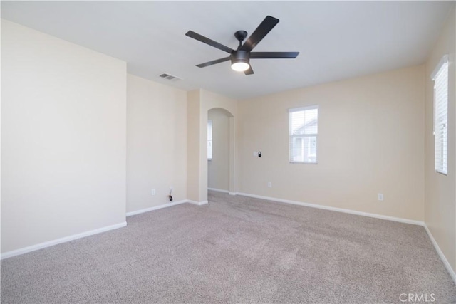 spare room featuring carpet floors, arched walkways, visible vents, a ceiling fan, and baseboards