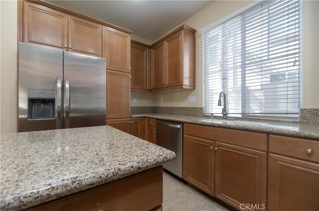 kitchen featuring light tile patterned floors, stainless steel appliances, light stone counters, and a sink