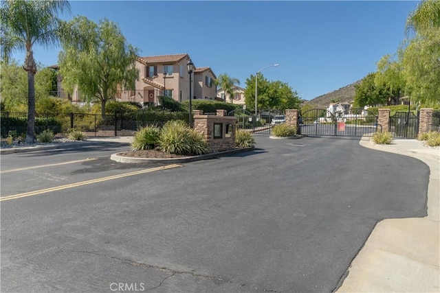 view of street featuring a gated entry, curbs, a gate, a residential view, and street lighting