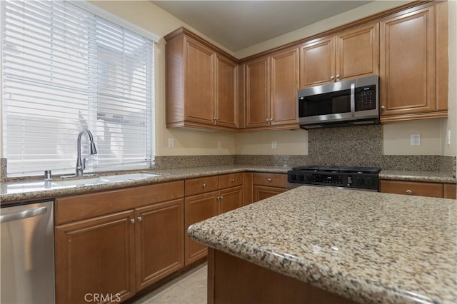 kitchen featuring stainless steel appliances, light stone counters, brown cabinetry, and a sink