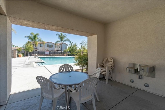 view of patio with outdoor dining space, fence, and a community pool