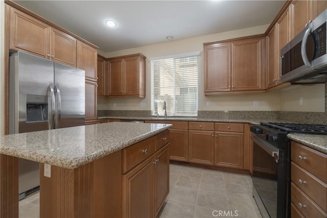 kitchen with appliances with stainless steel finishes, brown cabinetry, a sink, and light stone countertops