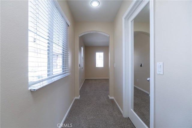 hallway featuring arched walkways, carpet floors, and baseboards