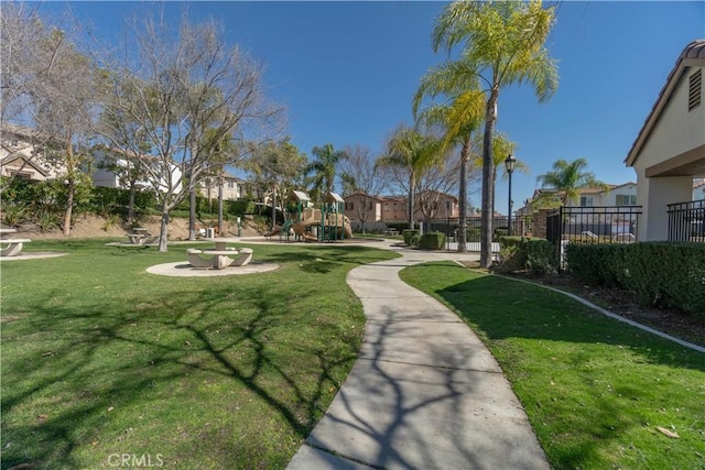 view of property's community featuring playground community, a lawn, fence, and a residential view