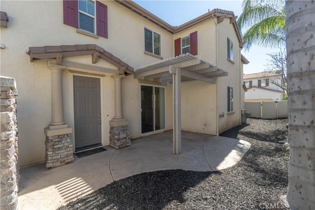 back of house with fence, stone siding, stucco siding, a pergola, and a patio area