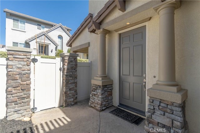 property entrance with stone siding, a gate, fence, and stucco siding