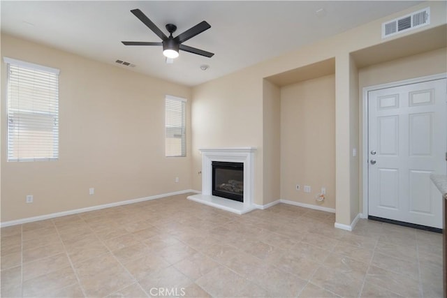 unfurnished living room featuring a glass covered fireplace, visible vents, ceiling fan, and baseboards