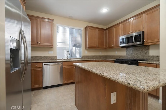 kitchen featuring light tile patterned floors, light stone counters, stainless steel appliances, a sink, and a center island