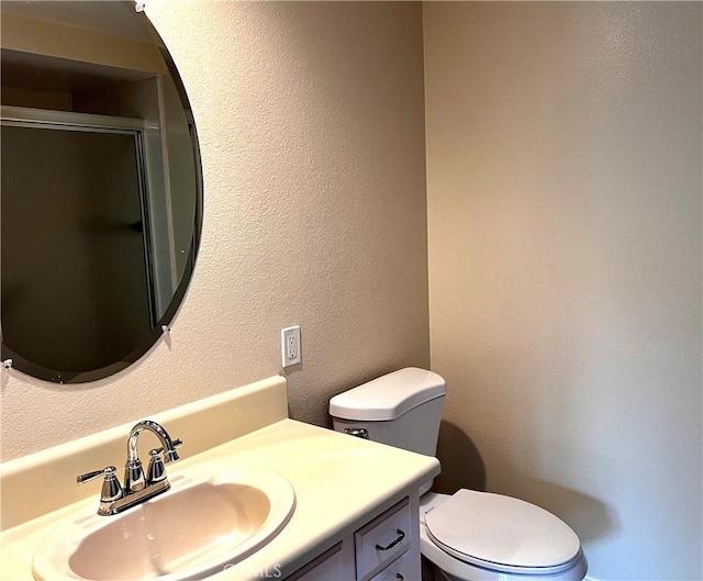 full bathroom with a stall shower, a textured wall, vanity, and toilet