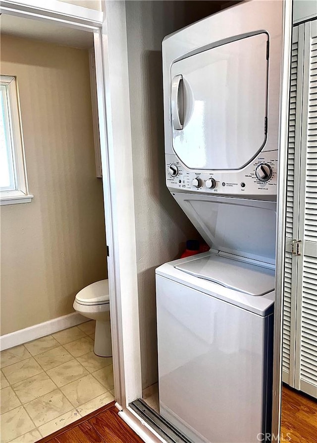 clothes washing area with stacked washer and dryer, tile patterned flooring, laundry area, and baseboards