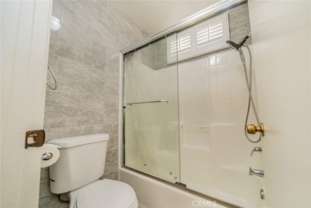 bathroom with enclosed tub / shower combo, toilet, and tile walls