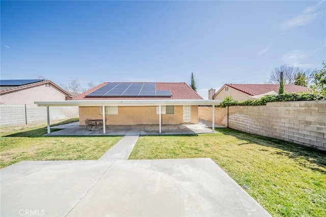 rear view of house with solar panels, stucco siding, a lawn, a patio area, and a fenced backyard