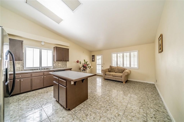 kitchen with lofted ceiling, freestanding refrigerator, a healthy amount of sunlight, a kitchen island, and a sink