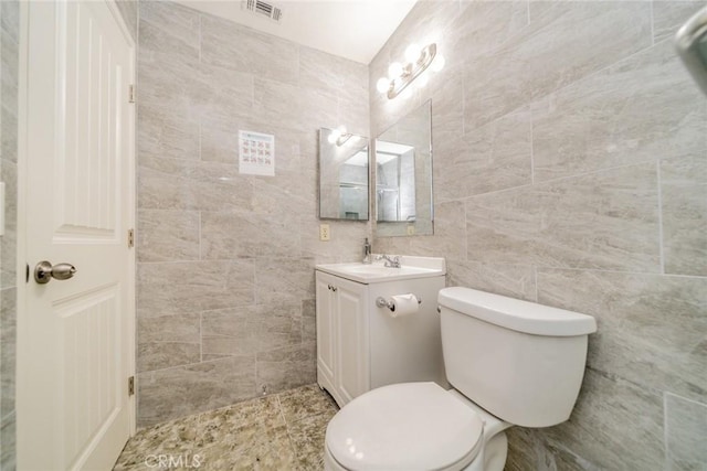 bathroom with tile walls, visible vents, vanity, and toilet