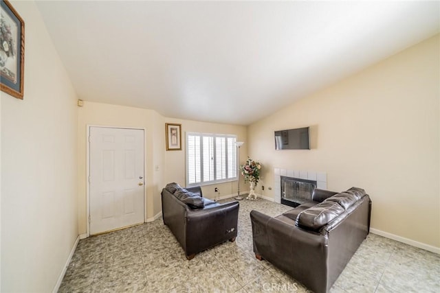 living room featuring baseboards, vaulted ceiling, and a tiled fireplace